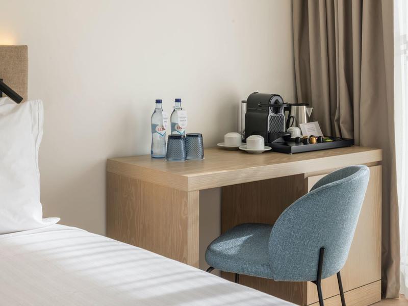 Modern hotel room area with desk, coffee machine, water bottles, and blue chair.