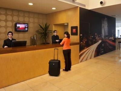 Hotelrezeption mit Tresen, zwei Mitarbeitern, einem Gast mit Koffer und moderner, heller Inneneinrichtung.