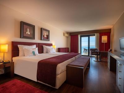 Modern hotel room with double beds, warm lighting, and a balcony with sea views.