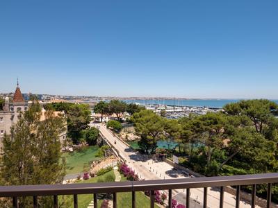 View from balcony showing lush garden, walkway, and distant sea under clear blue sky.