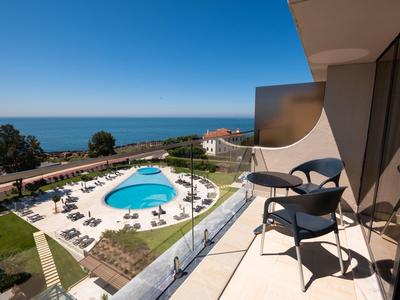 Balcony view of a coastal hotel with a pool, lounge chairs, and ocean in the background.