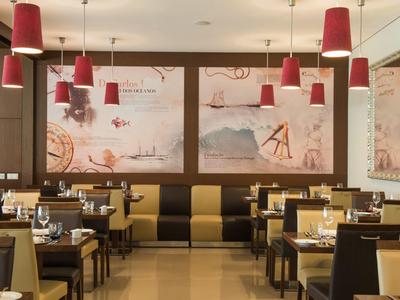 Modern restaurant with red pendant lights, wooden tables, and black and beige cushioned chairs.