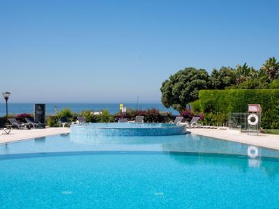 Großer Pool mit klarem blauem Wasser und Blick aufs Meer bei sonnigem Wetter.