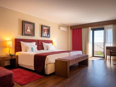 Modernes Hotelzimmer mit Doppelbett, Holzboden und Balkon mit Meerblick.