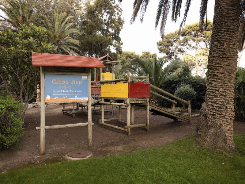 Outdoor playground with wooden structures and slides surrounded by palm trees and greenery.
