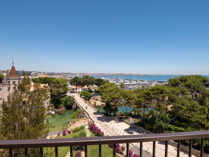 View from balcony showing lush garden, walkway, and distant sea under clear blue sky.