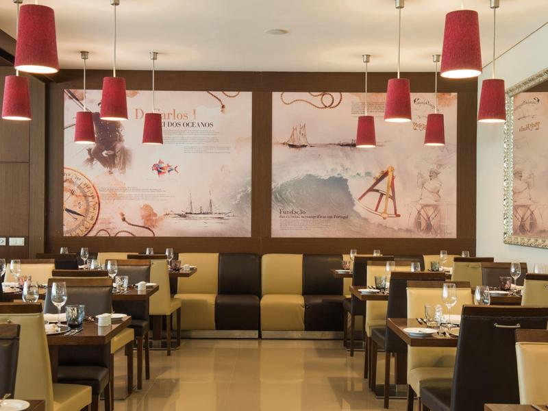 Modern restaurant with red pendant lights, wooden tables, and black and beige cushioned chairs.