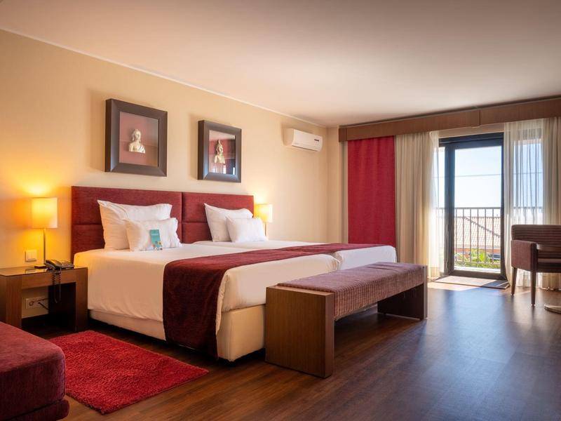 Spacious hotel room with a large bed, artwork, and balcony overlooking greenery.