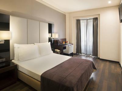 Bright hotel room with double bed, wooden floor, and balcony with curtains.