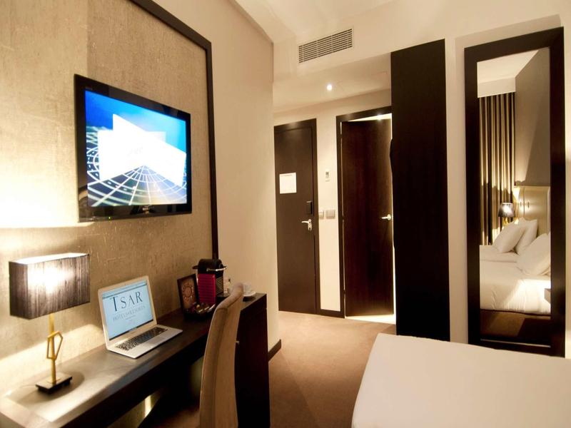 Modern hotel room with desk, TV, and bed in warm lighting.
