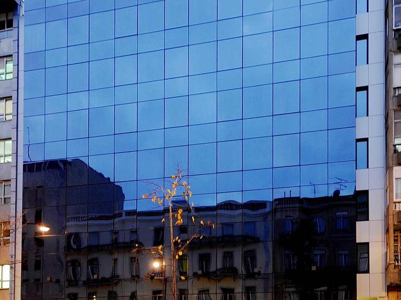 Modern glass facade of a multi-story building reflecting older architecture.