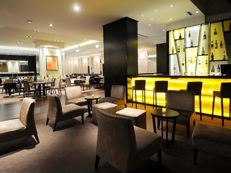 Modern bar and lounge area with illuminated counter, armchairs, and set tables.