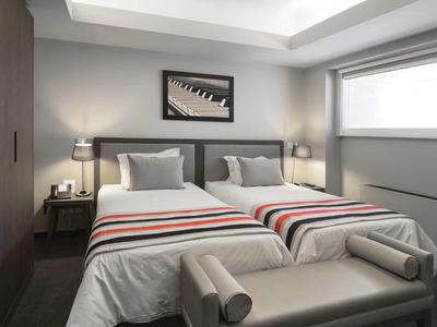 Modernes Schlafzimmer mit zwei Einzelbetten, grauem Polsterbank und großem Fenster.