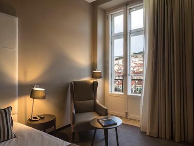 Gemütliches Schlafzimmer mit Sesseln, Nachttisch, Lampen und großen Fenstern mit Vorhängen.