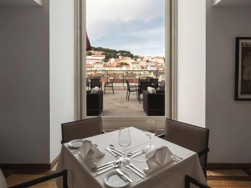 Moderner Essbereich mit eingedecktem Tisch vor großer Fensteröffnung und Stadtblick.