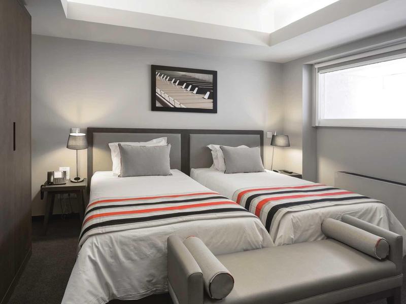 Modernes Schlafzimmer mit zwei Einzelbetten, grauem Polsterbank und großem Fenster.