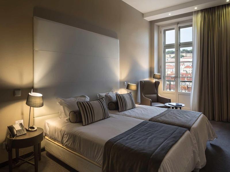 Gemütliches Hotelzimmer mit zwei Betten, Nachttischlampen und großem Fenster mit Blick auf Stadt.