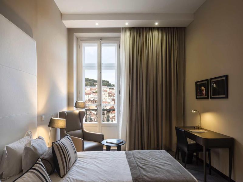 Modernes Schlafzimmer mit zwei Einzelbetten, großem Fenster, Schreibtisch und gedämpfter Beleuchtung.