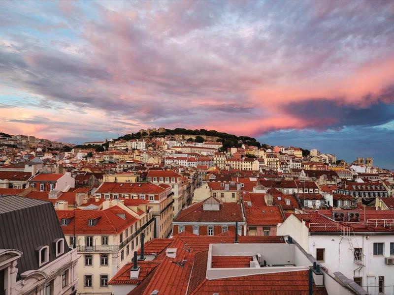 Stadt mit roten Dächern und Hügeln bei Sonnenuntergang unter bunt bewölktem Himmel.