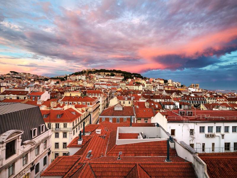 Stadtansicht mit vielen roten Ziegeldächern unter einem dramatischen Himmel bei Sonnenuntergang.