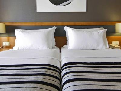 Twee eenpersoonsbedden met witte kussens en dekens, gestreepte bedspreien, nachtkastjes met lampen