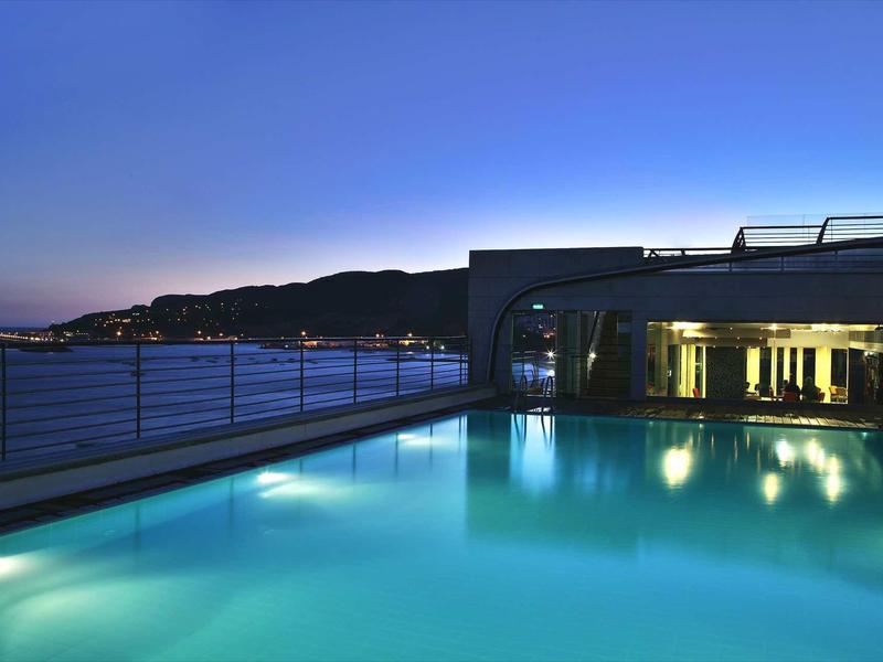 Verlichte zwembad op het dak met uitzicht op heuvels en zee bij zonsondergang.