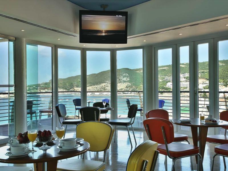 Moderne ontbijtruimte met glazen ramen met uitzicht op heuvels en water.