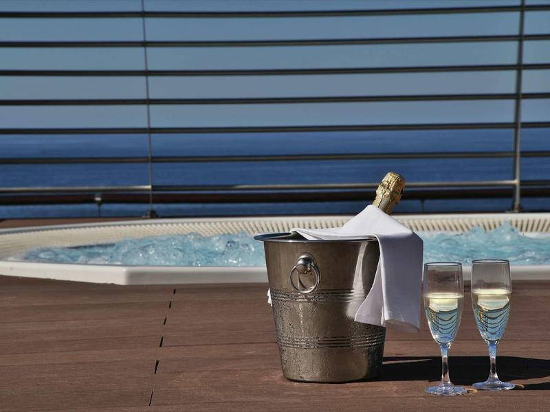 Champagnefles in een emmer met twee gevulde glazen op het dek bij het zwembad met uitzicht op zee