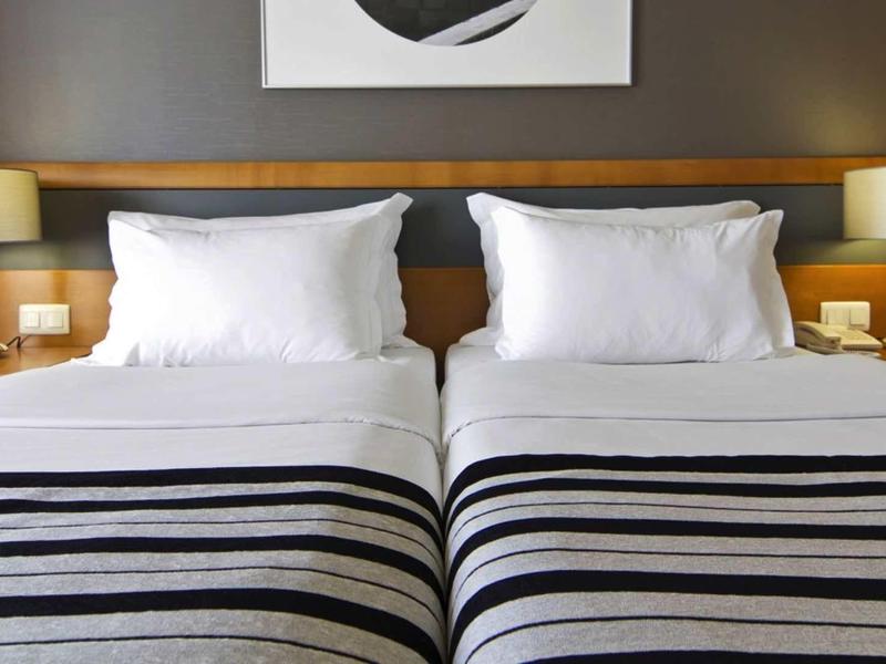 Twee eenpersoonsbedden met witte kussens en dekens, gestreepte bedspreien, nachtkastjes met lampen