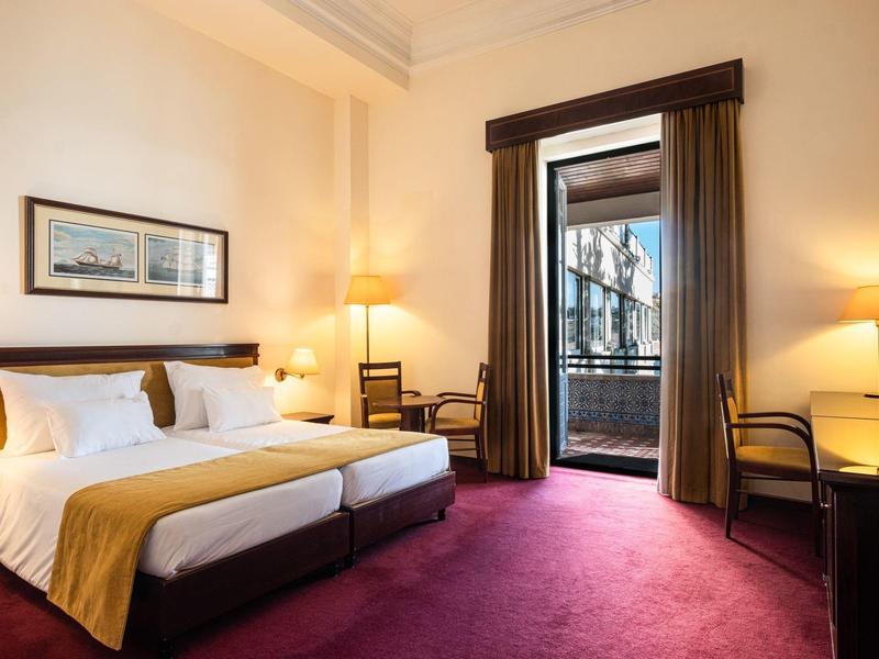 Elegantní hotelový pokoj se dvěma oddělenými postelemi, fialovým kobercem a otevřeným balkonem.