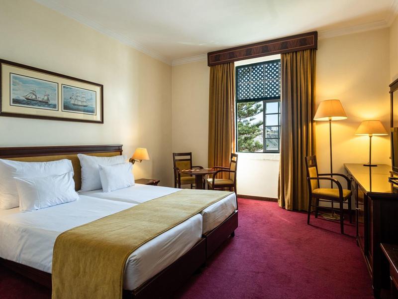 Pohodlný hotelový pokoj se dvěma jednolůžky, červeným kobercem a dřevěným nábytkem.