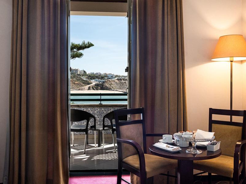 Hotelový pokoj se stolem, šálky, židlemi a balkonem s výhledem do slunečného exteriéru.