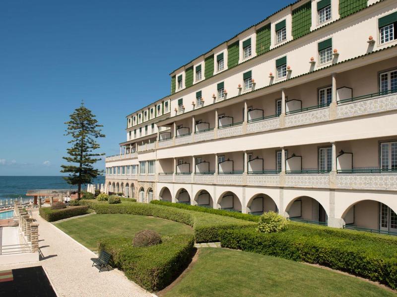 Elegantní hotel u moře s zeleným trávníkem a čistou modrou oblohou.