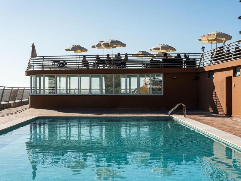 Venkovní bazén s lehátky a slunečníky na slunné terase.