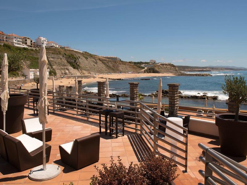 Slunečná terasa s křesly a slunečníky s výhledem na moře a útes v pozadí.