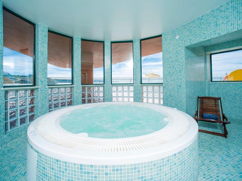 Kruhové vířivka v místnosti s modrými dlaždicemi a širokými okny.