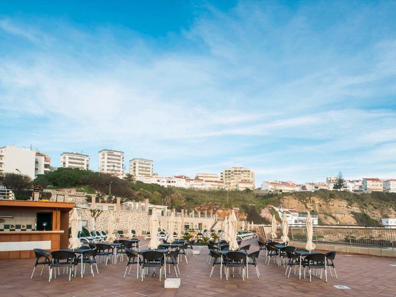 Terasa s stoly a židlemi s výhledem na město na kopci pod jasnou modrou oblohou.