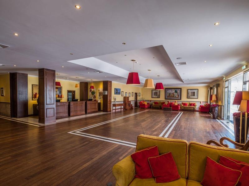 Prostorný hotelový salonek se žlutými křesly, červenými pohovkami a dřevěnou podlahou.