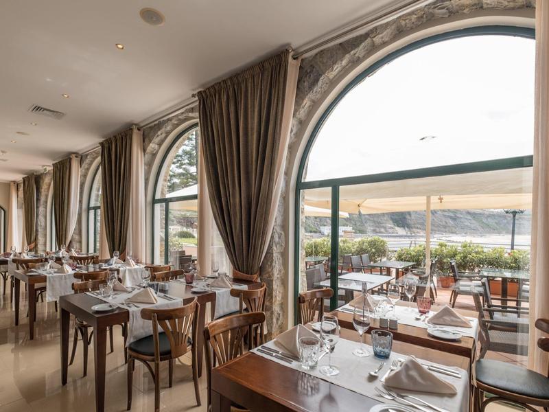 Elegantní restaurace s velkými oblouky a výhledem na terasu a moře.