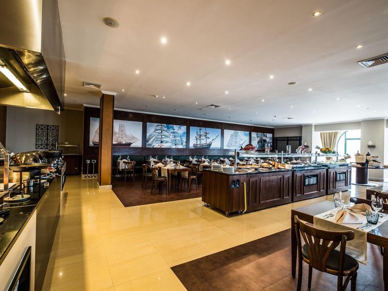 Moderní hotelová restaurace s prostřenými stoly a centrálním bufetem za teplého osvětlení.