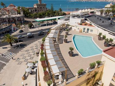 Vista de un hotel con piscina y tumbonas, y el mar al fondo bajo un cielo despejado.