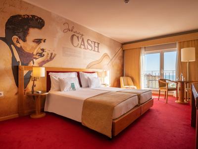 Habitación de hotel acogedora con cama grande, arte en la pared y balcón con vista exterior.