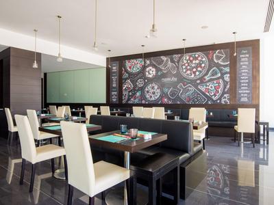 Moderna sala de restaurante con sillas blancas, bancos negros y amplio ventanal.