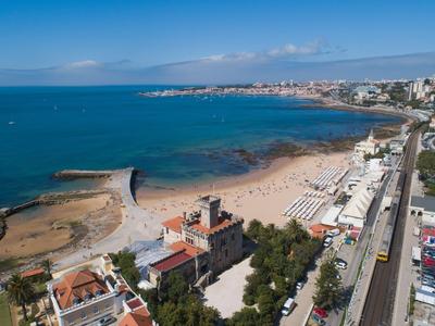 Vista de una gran playa de arena y el mar, con una ciudad al fondo y una carretera a la derecha.