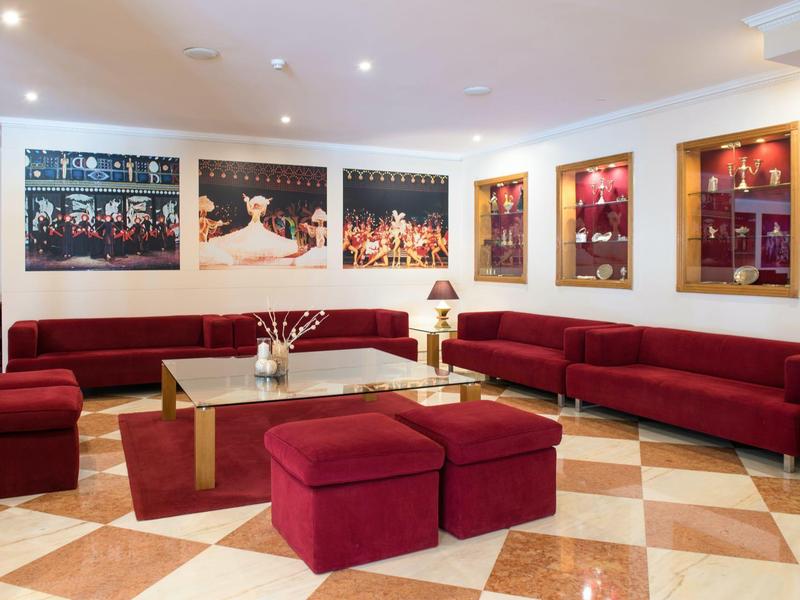 Área elegante del vestíbulo del hotel con sofás rojos, suelo de mármol y cuadros decorativos en la pared.