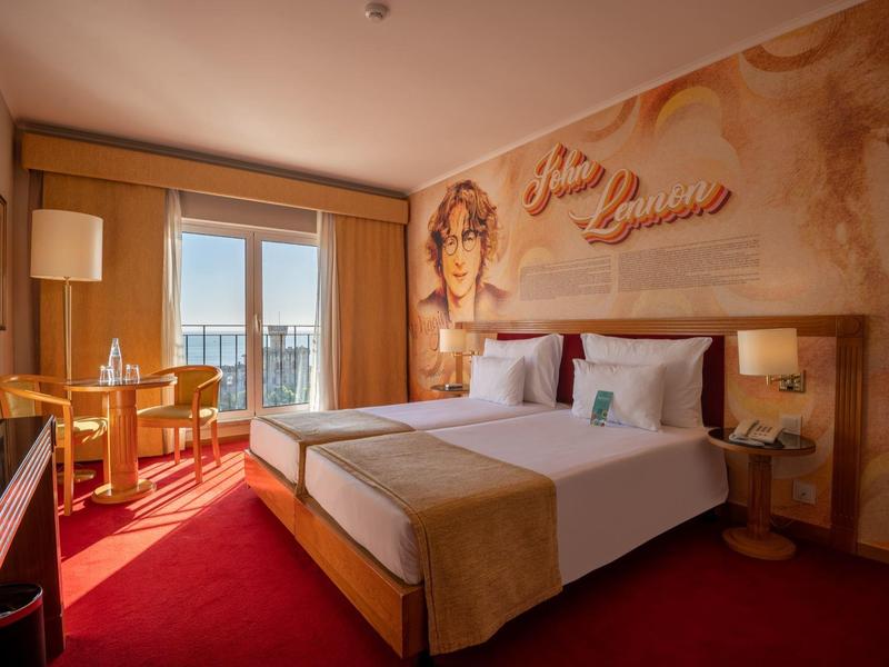 Habitación de hotel luminosa con cama doble, arte mural y balcón con vista al agua.