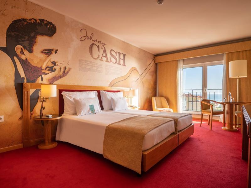 Habitación de hotel acogedora con cama grande, arte en la pared y balcón con vista exterior.