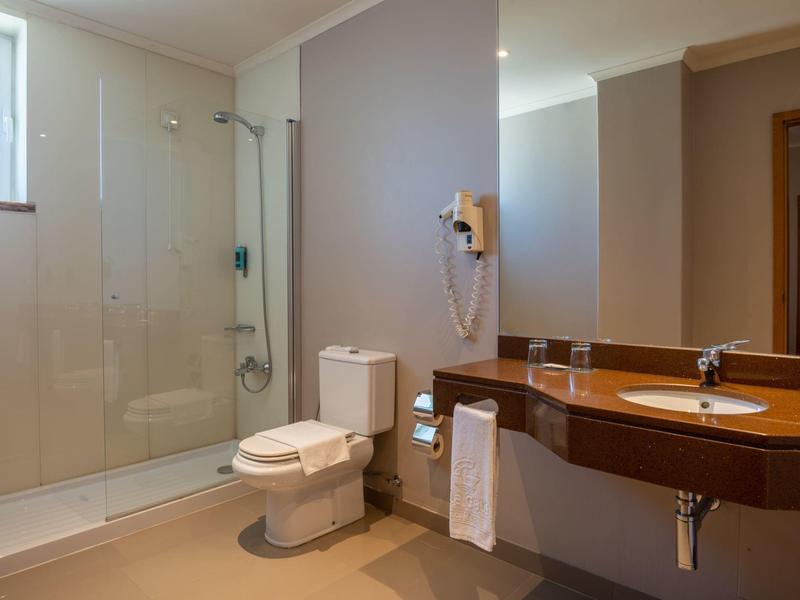 Baño moderno con ducha de vidrio, inodoro y lavabo con espejo y toallas.