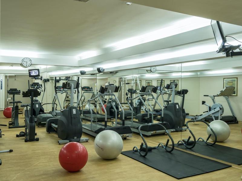 Gimnasio moderno con varios equipos de ejercicio y pelotas de gimnasia frente a un espejo.