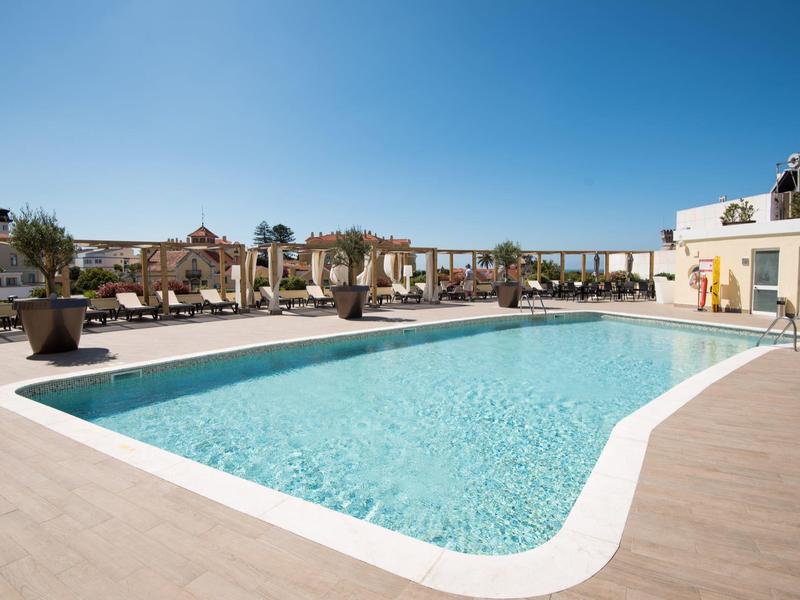 Piscina azul clara en terraza de madera con tumbonas bajo cielo despejado.
